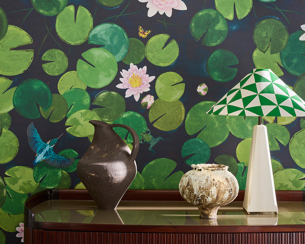 Decorative table with a vase, lamp, and small sculpture against Little Greene Lily Pads Mural Wallpaper