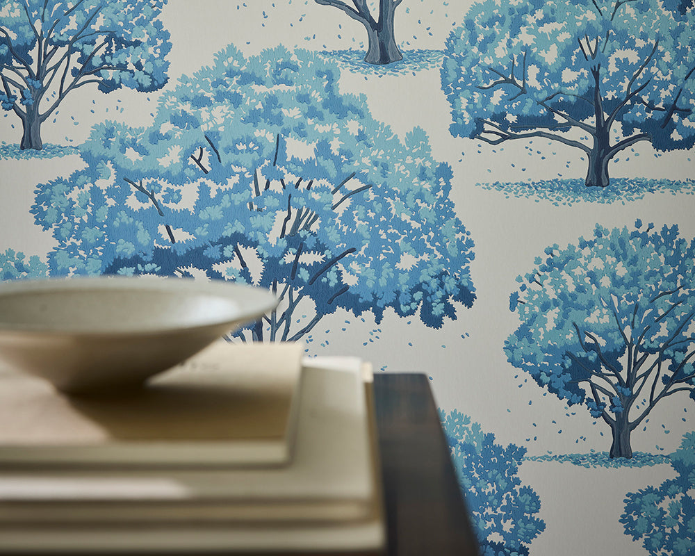 Side table setting with bowl against the blue tree-patterned Little Greene Magnolia Blossom Wallpaper.