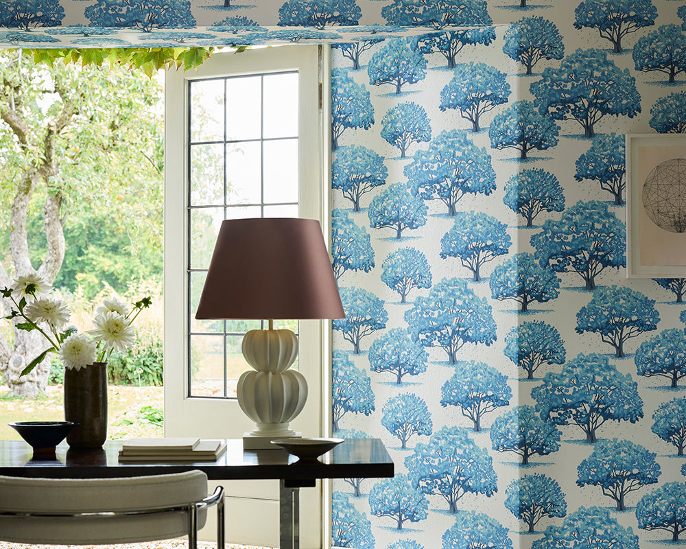 Room interior with a table, lamp, and decorative Little Greene Magnolia Blossom Wallpaper featuring blue tree patterns.