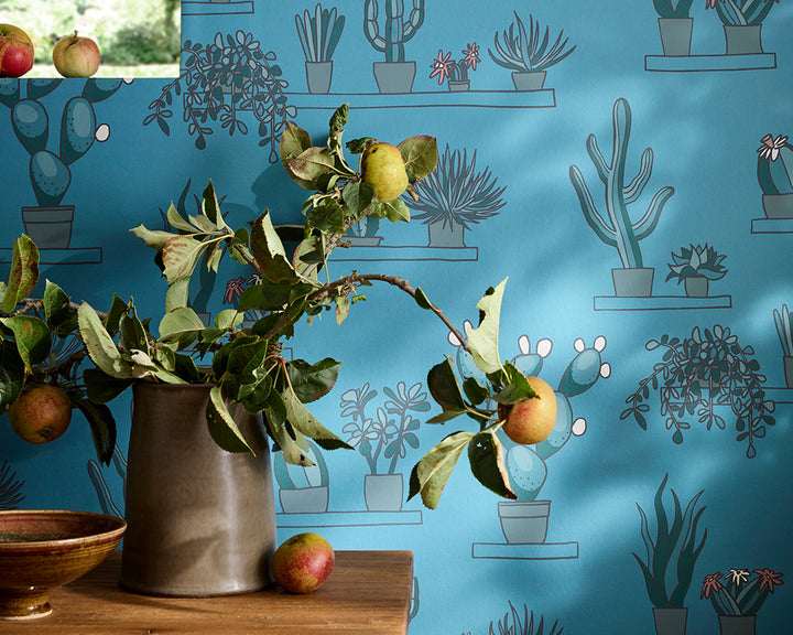 Vase with apple branch and apples on a table against the blue Little Greene Mr Straw's Greenhouse Wallpaper with plant patterns