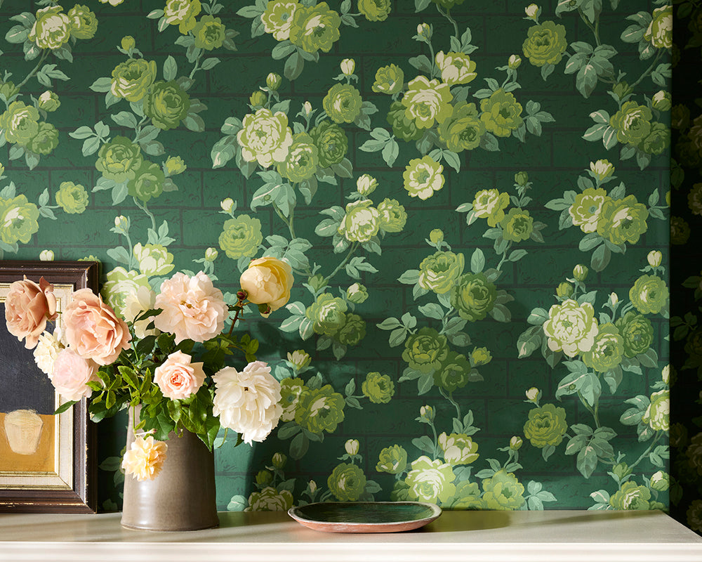 Little Greene Rose Garden, floral wallpaper with green and white flowers on a dark green background, with a vase of flowers and a framed picture in the foreground.