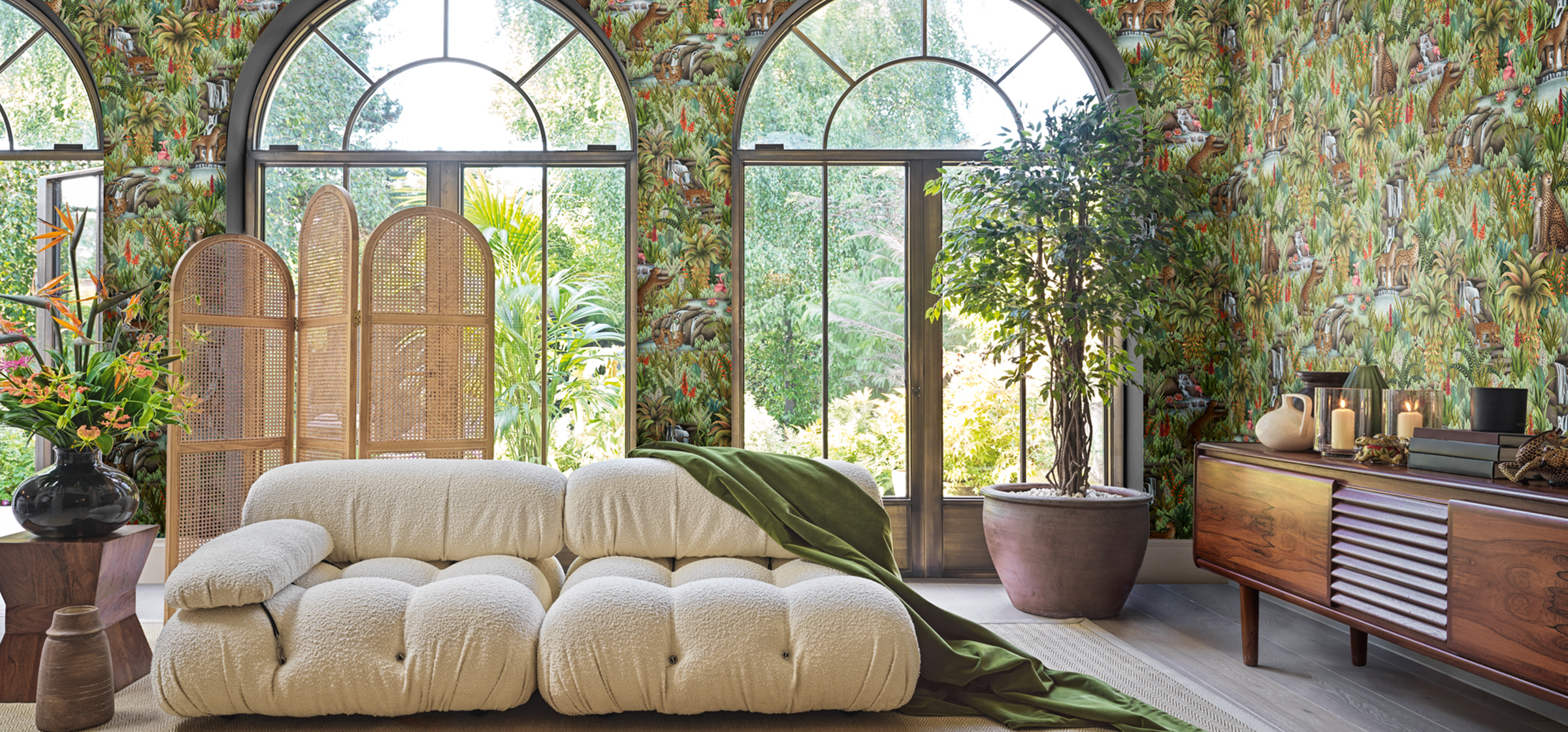 Decorative living room with a beige sofa, floral Cole Son x Ardmore Injisuthi wallpaper, and large windows.