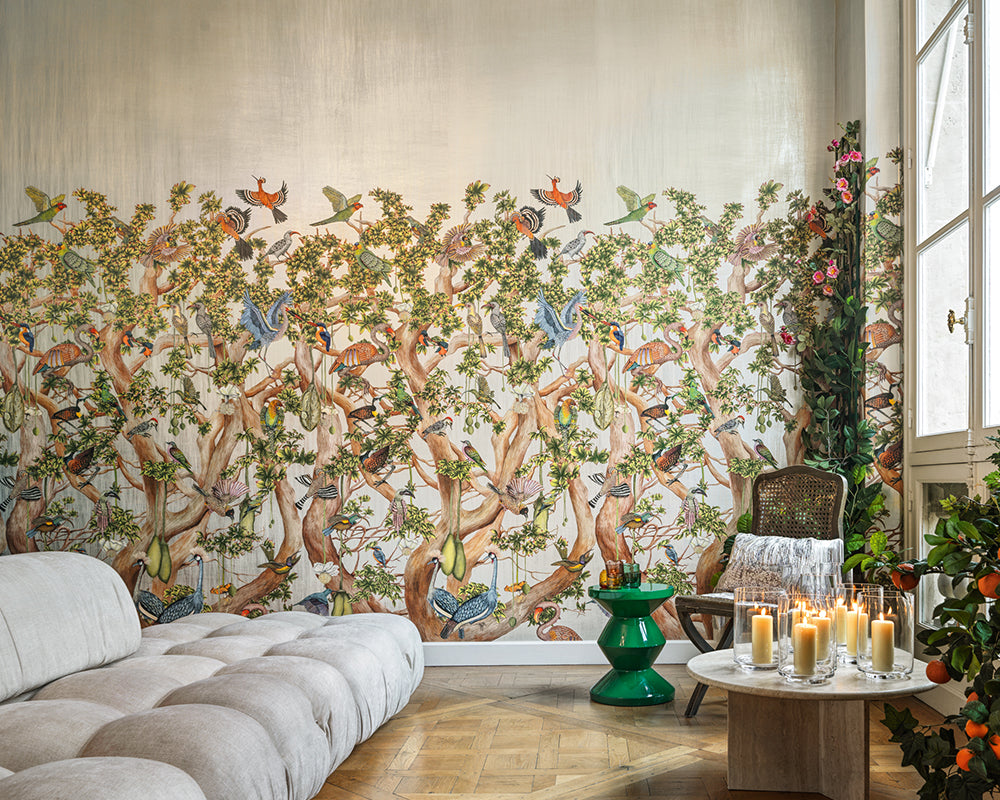 Living room with a decorative wall mural Cole & Son Tree of Life Wallpaper - Platinum featuring trees and birds, a white sofa, and a coffee table with candles.