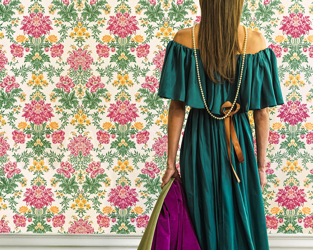 Woman in a green dress holding a purple bag against the floral Cole & Son Poppies Wallpaper