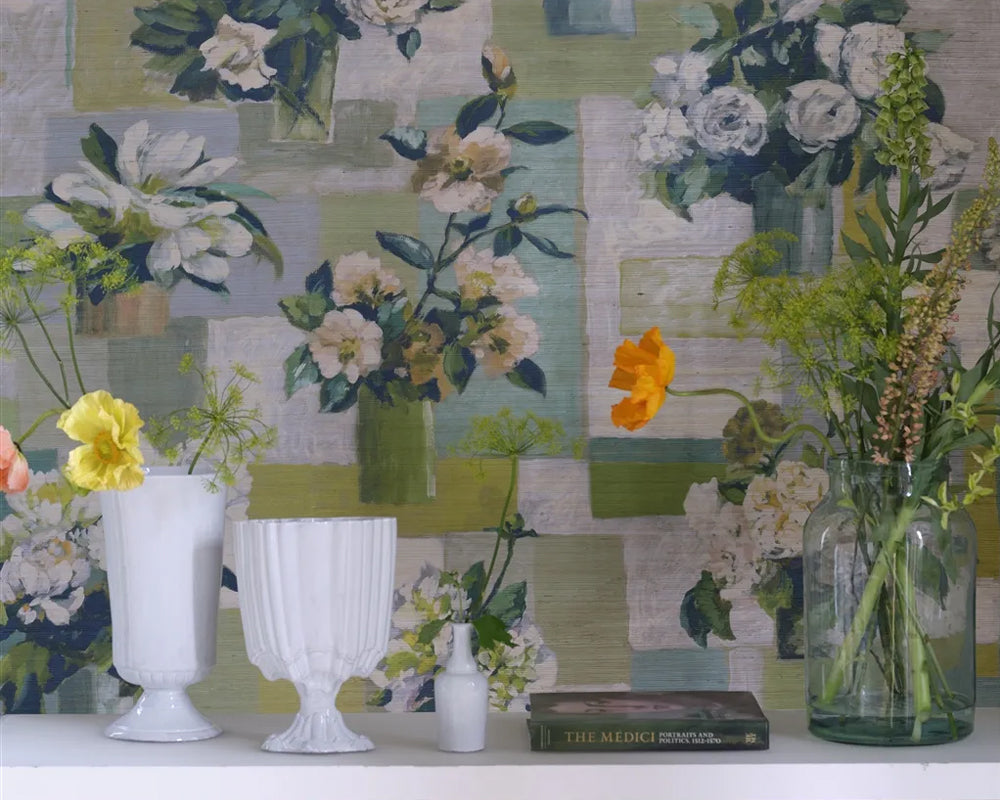 Decorative setting with vases, flowers, and a book against the floral-patterned Designers Guild Celadon Vase Wallpaper on Grasscloth