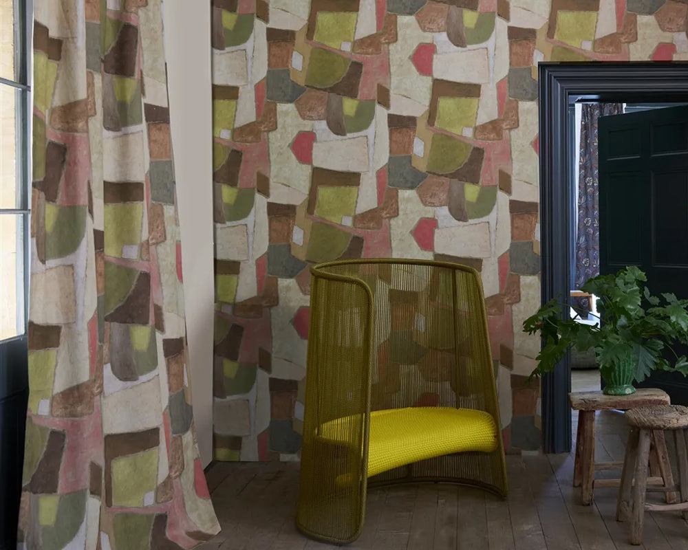 Room with patterned curtains, a yellow chair, and a plant set against Designers Guild Clay Collage Wallpaper