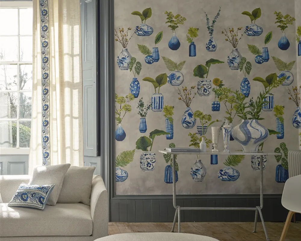 Living room with decorative Designers Guild Kawana Wallpaper featuring blue vases and green plants.