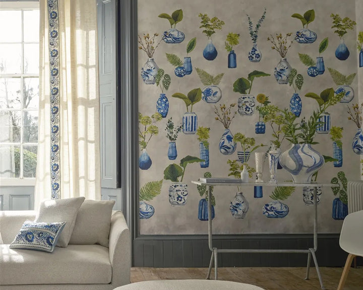 Living room with decorative Designers Guild Kawana Wallpaper featuring blue vases and green plants.