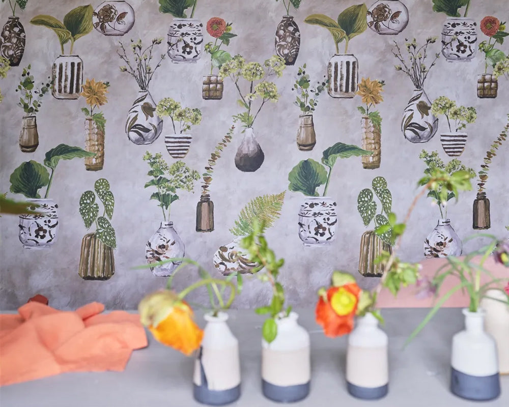 Decorative Designers Guild Kawana Wallpaper with plant and vase patterns, featuring small vases and flowers on a gray background.
