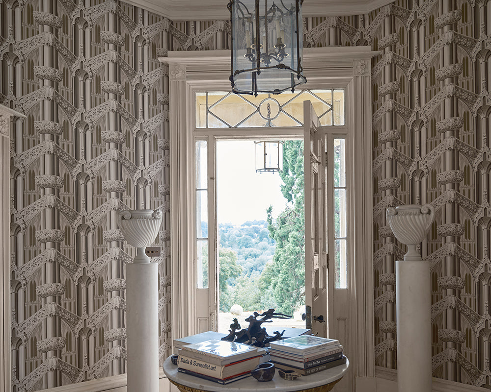 Elegant Farrow & Ball Gothic wallpaper featuring a repeating classical architectural pattern in beige and gray, styled in a luxurious room with white columns, a round table with books, and an open window looking out to trees.