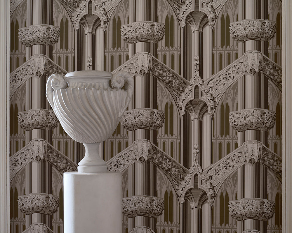 A white classical-style urn on a pedestal in front of ornate repeating Gothic arch and tracery wallpaper, Farrow & Ball Gothic, in warm beige and taupe tones.
