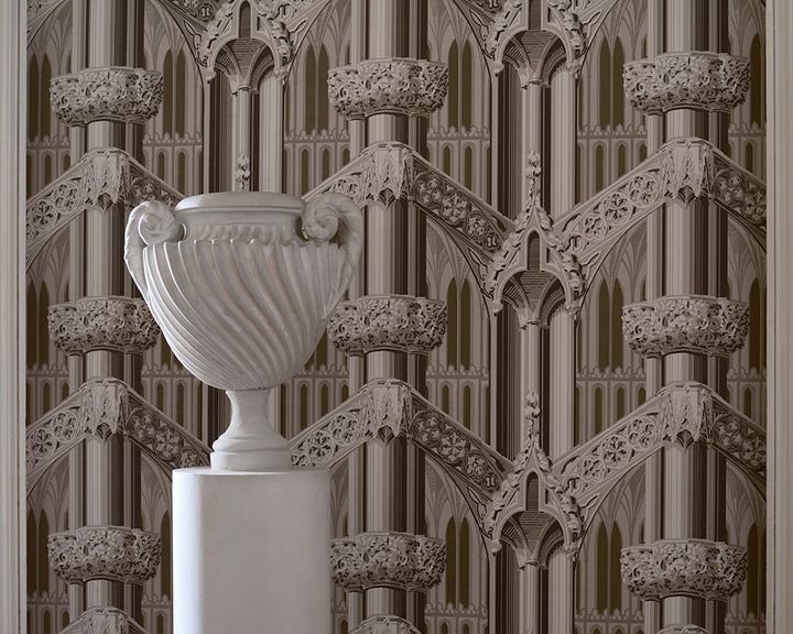 A white classical-style urn on a pedestal in front of ornate repeating Gothic arch and tracery wallpaper, Farrow & Ball Gothic, in warm beige and taupe tones.