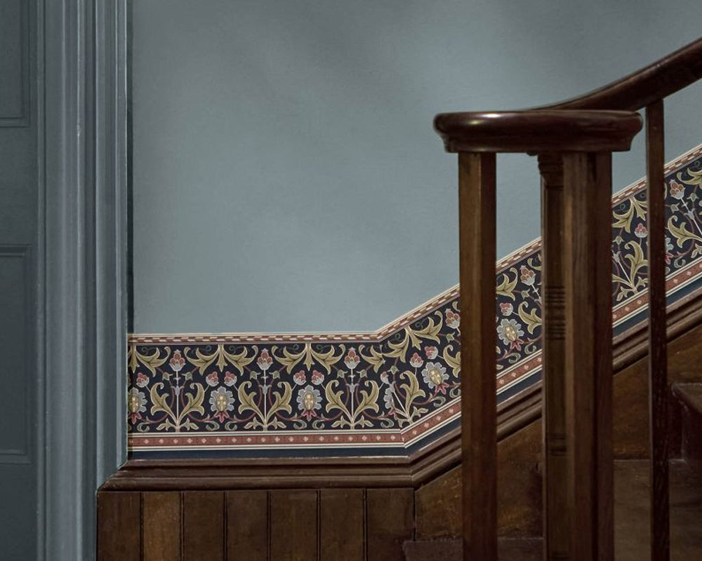 An ornate floral wallpaper border with a dark navy and golden pattern, installed along a wooden staircase against a muted blue-gray wall.