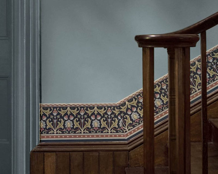 An ornate floral wallpaper border with a dark navy and golden pattern, installed along a wooden staircase against a muted blue-gray wall.