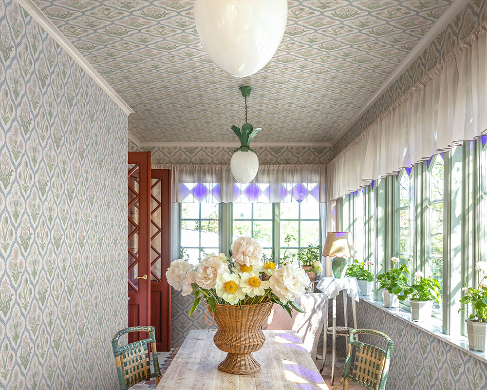 Sandberg Rosa Wallpaper in a dining room with floral arrangement on a table, large windows, and decorative elements.