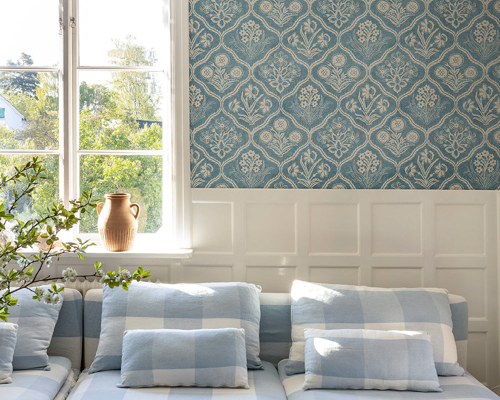 Sandberg Rosa Wallpaper in a living room interior with blue and white checkered sofa and a window with greenery outside.